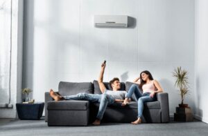 young-couple-sits-on-couch-changes-temperature-on-mini-split-behind-them